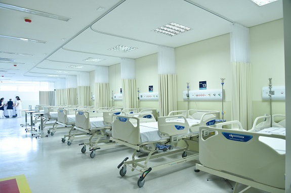 Foto mostra alguns dos leitos do hospital em tons bege claro e cortinas divisórias entre eles na mesma cor.