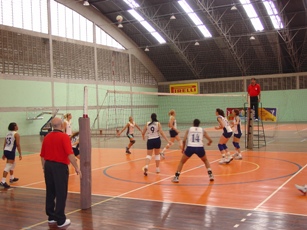 Imagem mostra jogo de voleibol em quadra de ginásio fechado