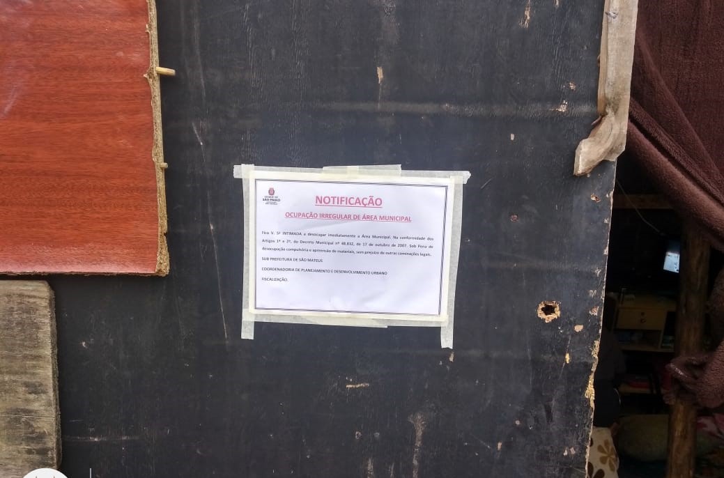 Notificação colada em outra construção precária, de madeira, solicita a retirada imediata de todo o material