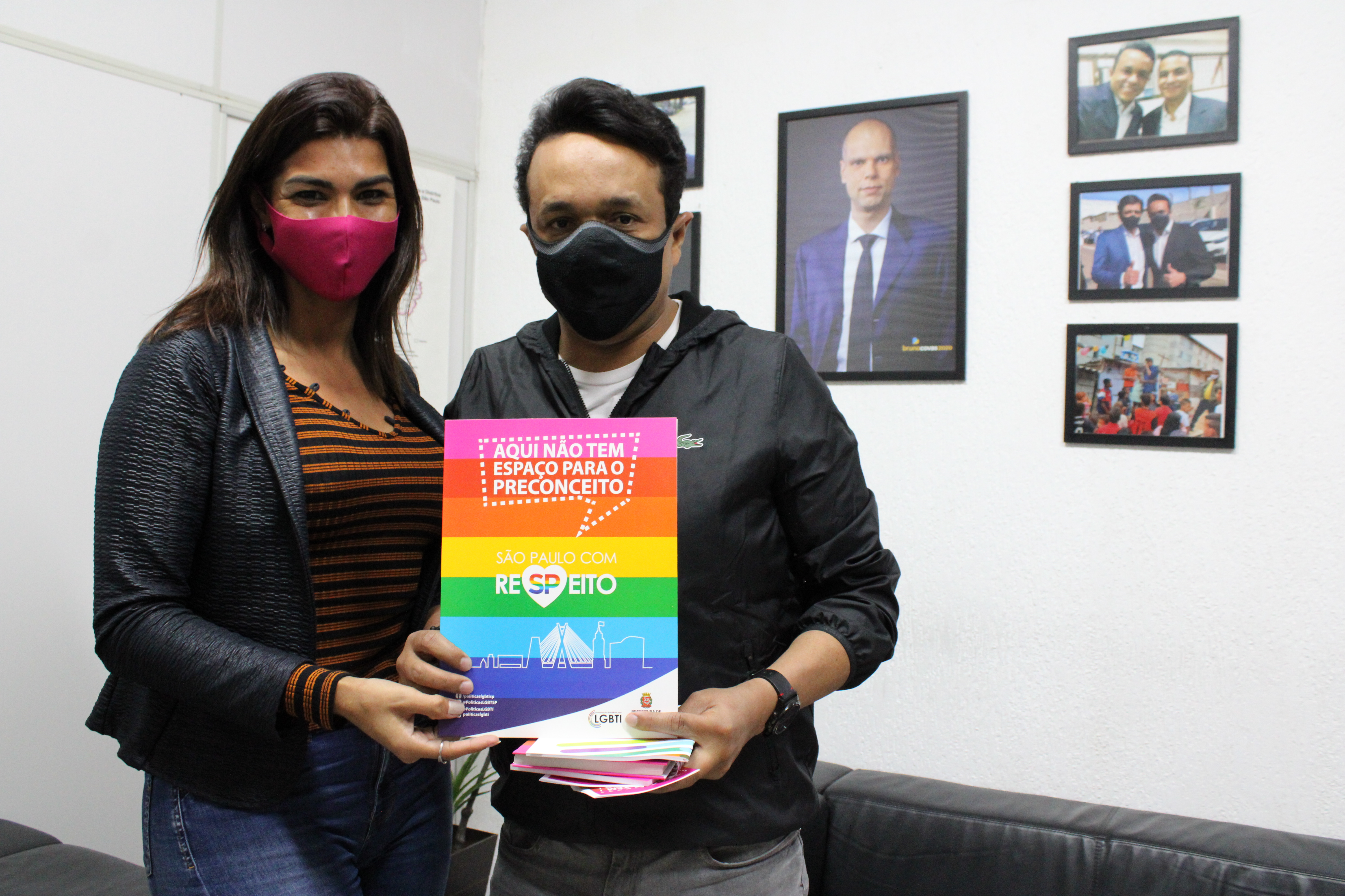 Na imagem está a secretária Gabriella Bueno ao lado do subprefeito Gilmar Santos em pé segurando um cartaz com as cores do arco-íris com a frase "aqui não tem espaço para o preconceito".