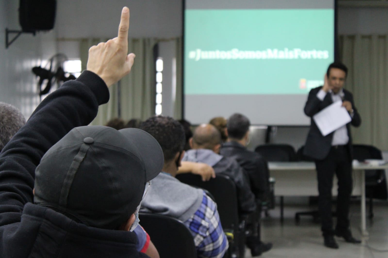 No primeiro plano da imagem aparece um servidor da Subprefeitura Itaim Paulista com o mão levantada, na reunião do mutirão das podas de árvores.