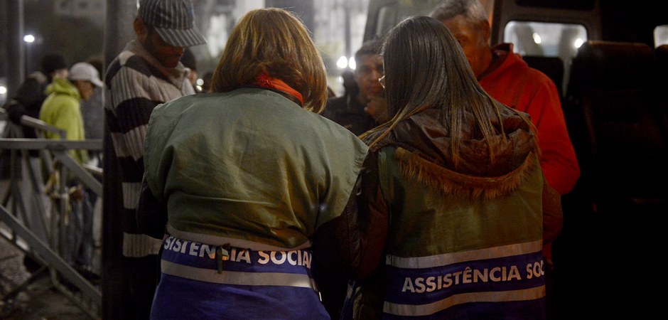 Foto colorida de duas funcionárias da Prefeitura prestando o serviço de assistência social a moradores de rua