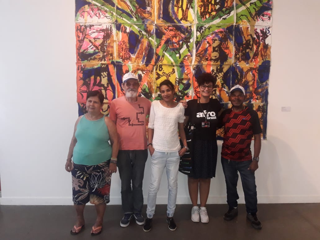 Quatro conviventes aparecem sorrindo ao lado da guia do museu que veste uma camiseta escrito Afro Brasil
