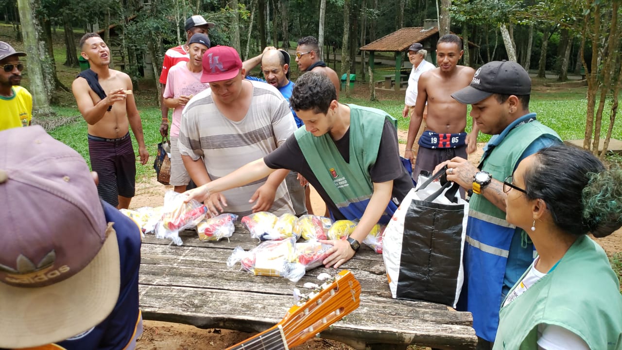 Homem com um colete com o logo da Prefeitura de São Paulo distribuindo kits com lanches para os conviventes