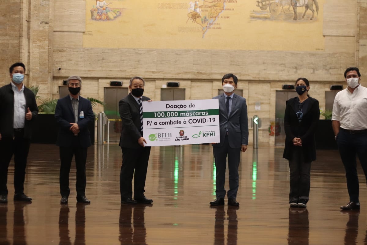 Participantes postam com uma placa com a frase de doação de 100 mil máscaras