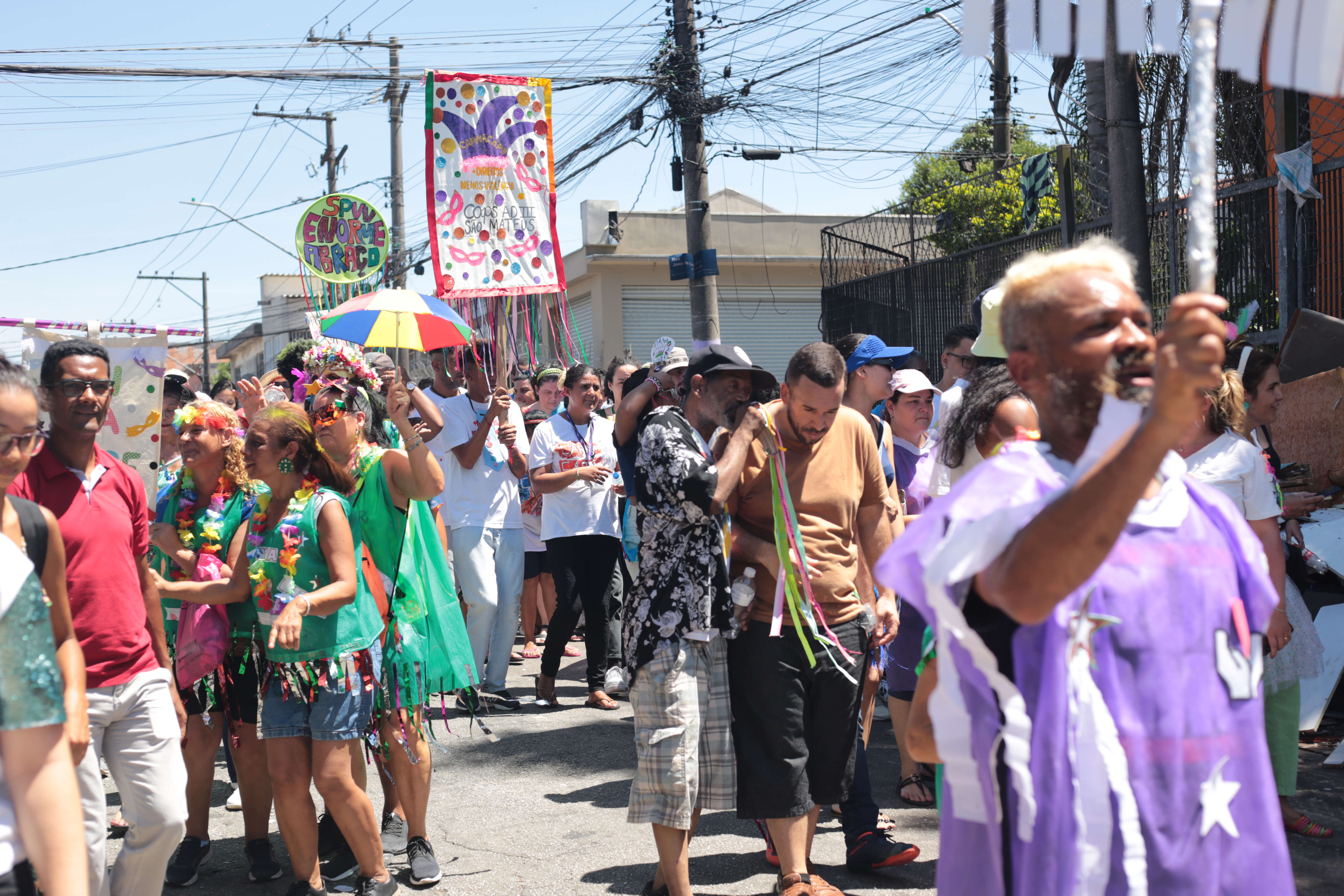 A foto mostra pessoas da comunidade, homens e mulheres, de diversas idades, fantasiadas e espalhadas pela rua durante o CarnaCaps.