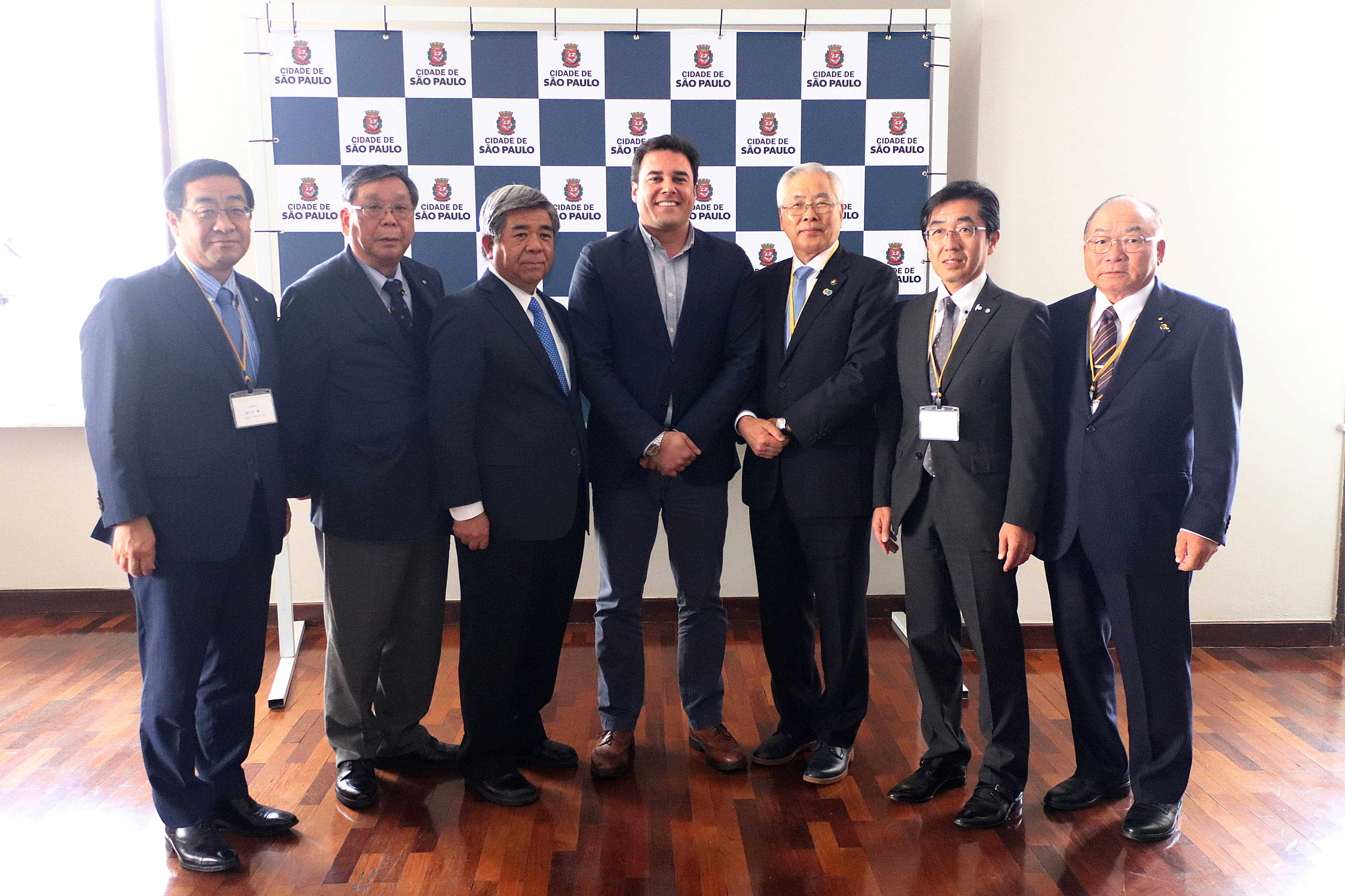 Secretário Luiz Alvaro ao lado dos Prefeitos da Província de Hokkaido (Japão). Ao fundo, um backdrop com o logotipo da Prefeitura de São Paulo.
