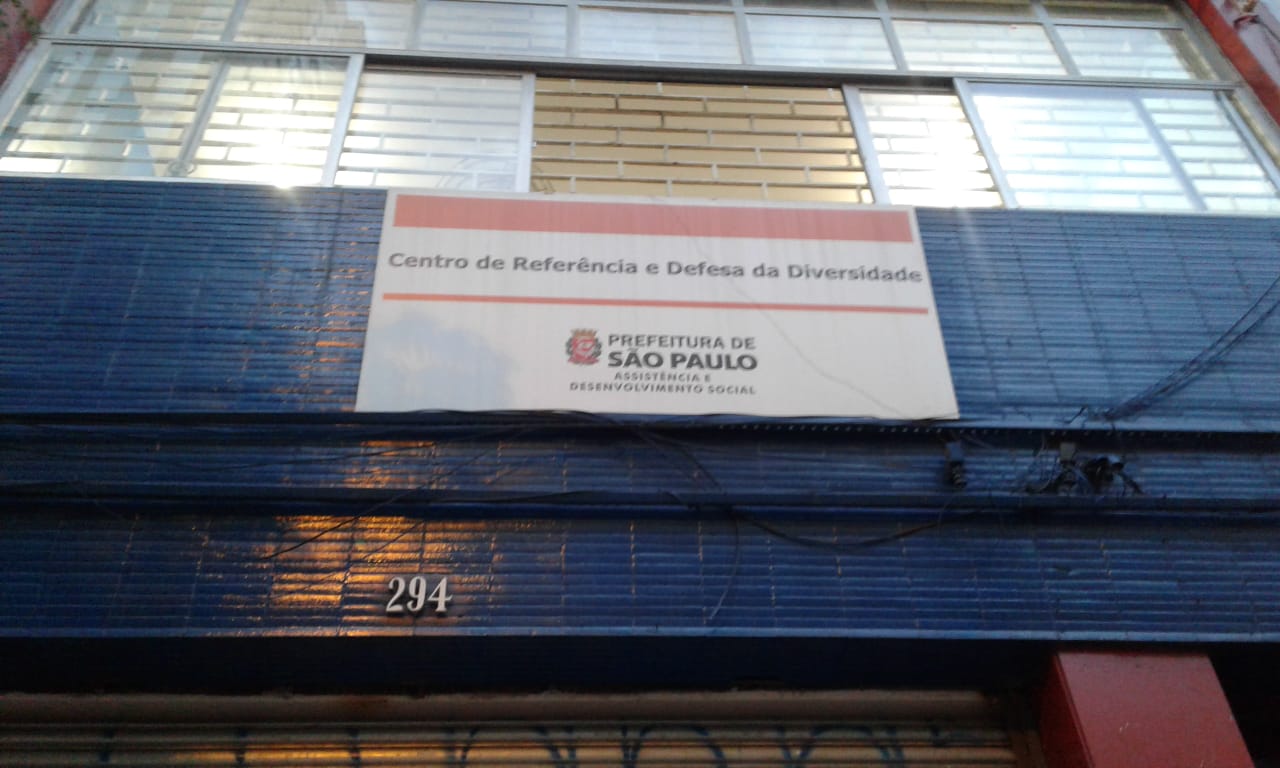 Placa do serviço vista de baixo, onde se lê Centro de Referência e Defesa da Diversidade, Prefeitura de São Paulo, Assistência de Desenvolvimento Social 