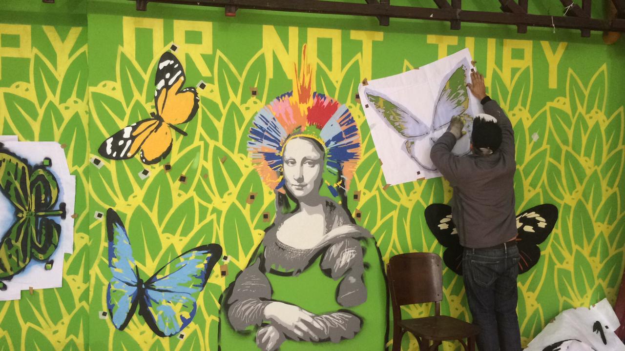 Um murro está sendo colorido por um homem de costas, com a imagem da obra de arte da Monalisa e borboletas.
