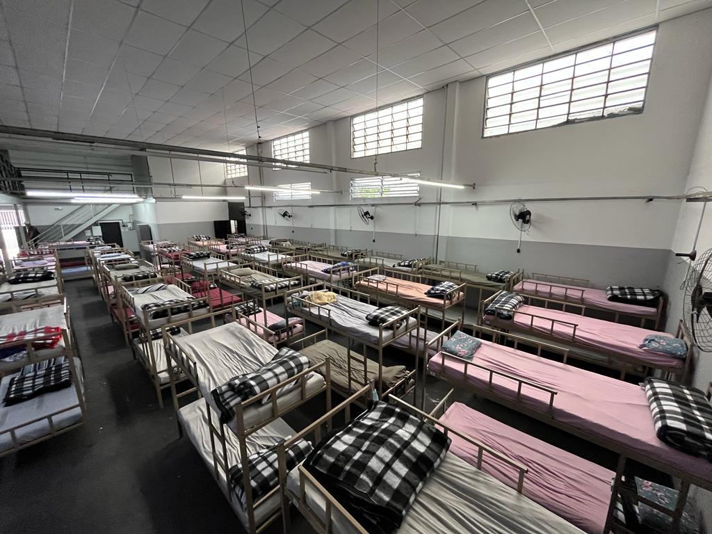 Na foto, tirada do alto, mostra seis fileiras de camas, todas arrumadas com roupas de camas de diferentes cores.