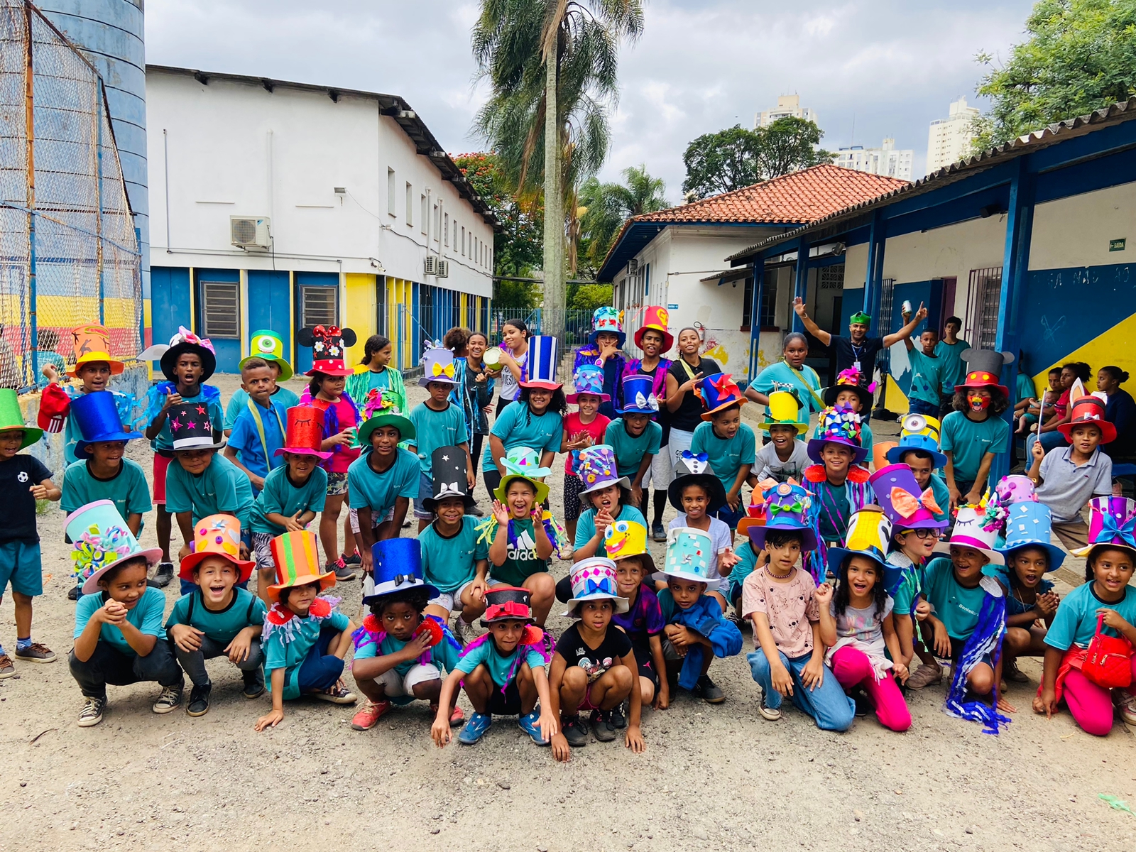 Crianças posam para a foto com roupas carnavalescas. Todas estão com camisetas azuis e usam chapéus coloridos com laços