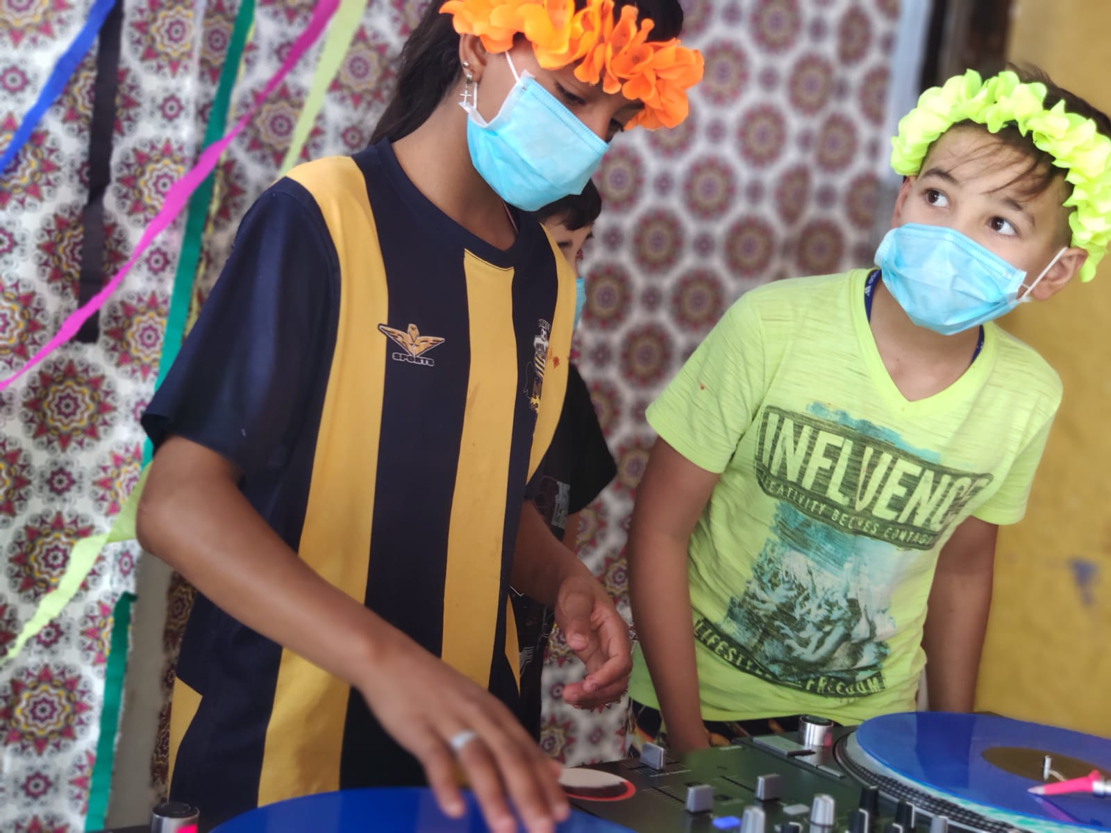 Duas crianças de máscara mexendo nos aparelhos de mixagem de DJ 