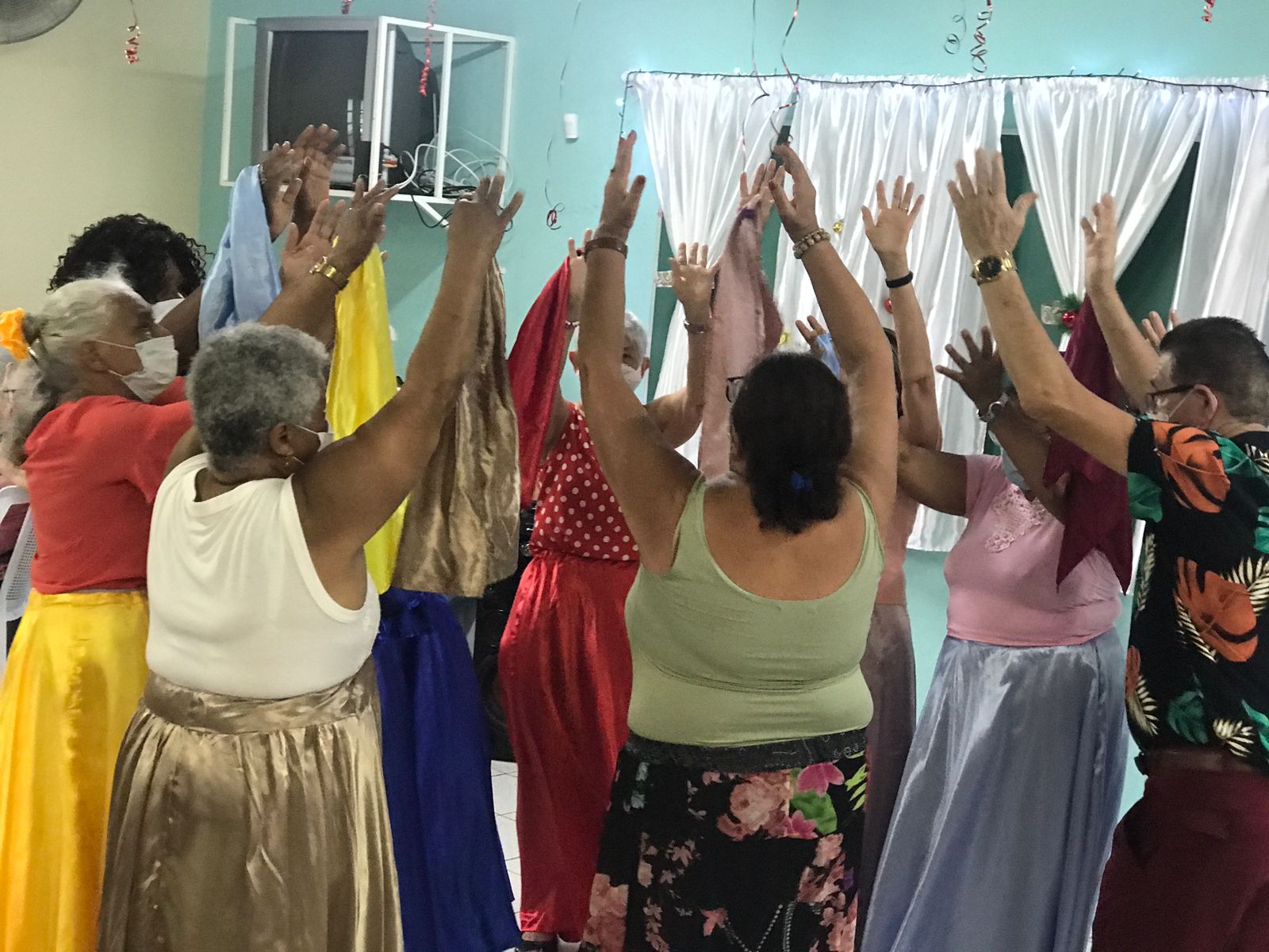  Senhoras com saias coloridas e braços pra cima fazendo a apresentação de dança circular