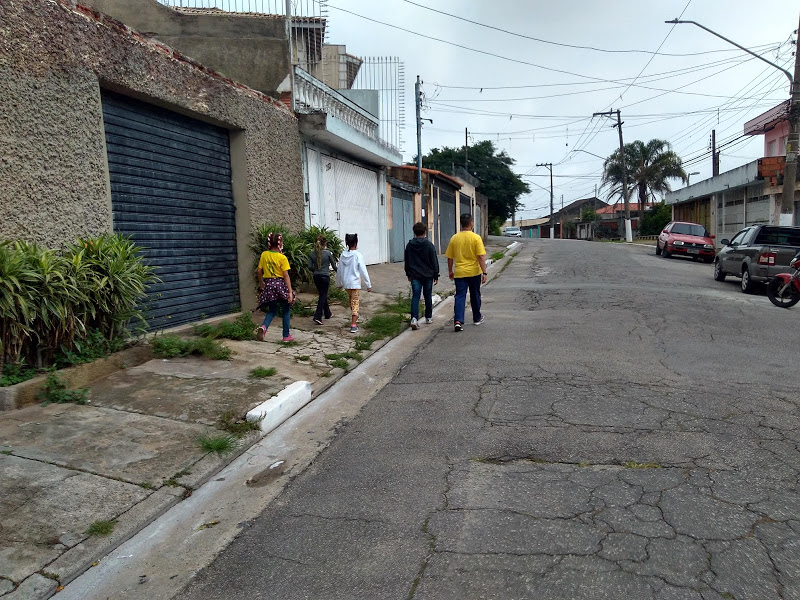 Foto de cinco atendidos pelo CCA caminhando pela rua durante os passeios. Eles estão do lado esquerdo da calçada, de costas para a imagem