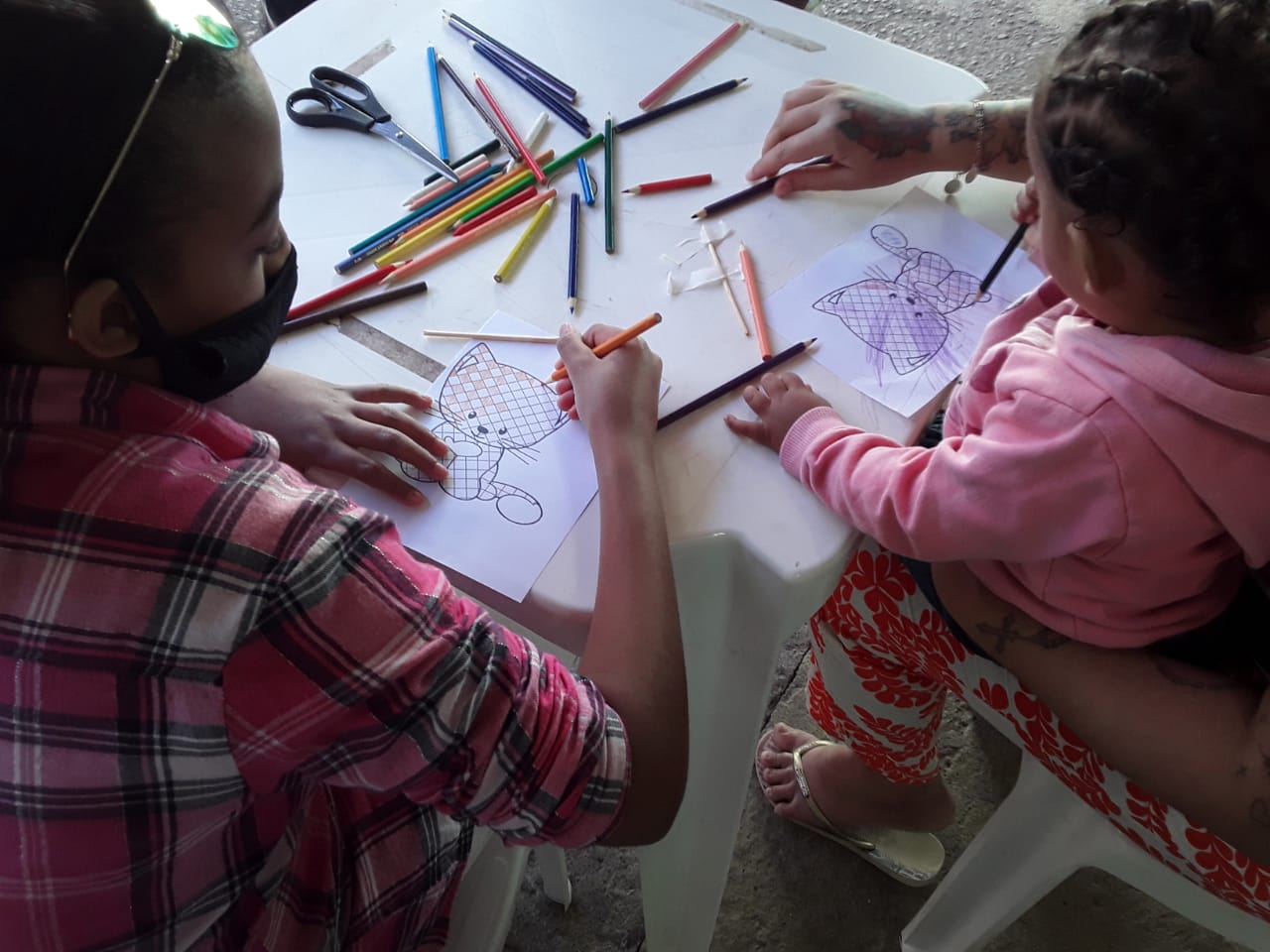 Em uma mesa do SASF estão duas crianças pintando os desenhos de gatos xadrez com lápis de cor