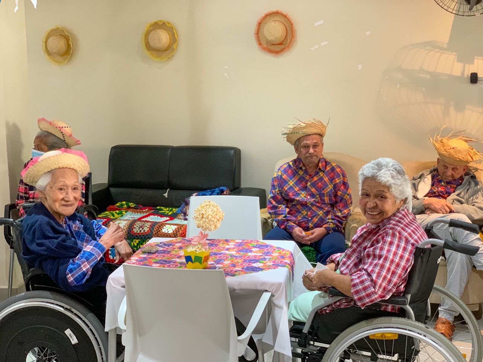 Na imagem aparecem quatro idosos sentados em uma mesa, vestidos de xadrez. 