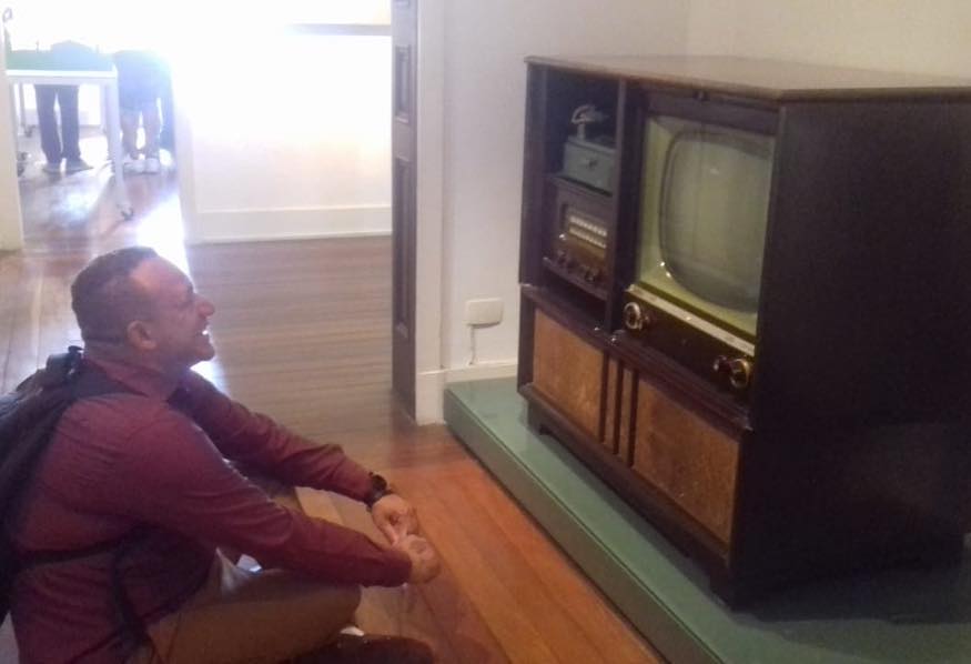 Usuário do serviço sentado no chão enquanto olha uma televisão antiga em exposição no museu 