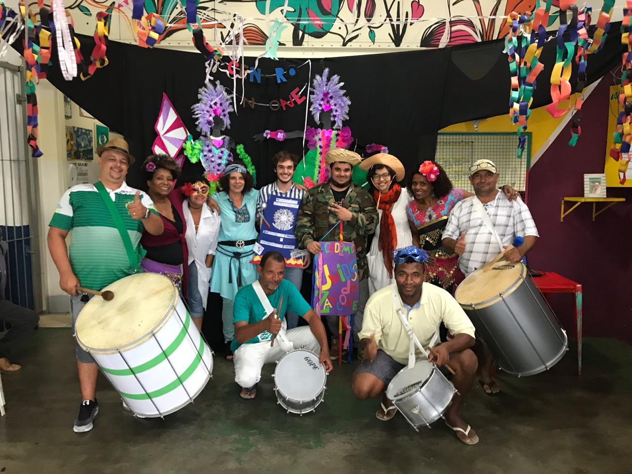 Em um espaço todo decorado de carnaval, conviventes, convidados e funcionários posam para foto com instrumentos de percussão