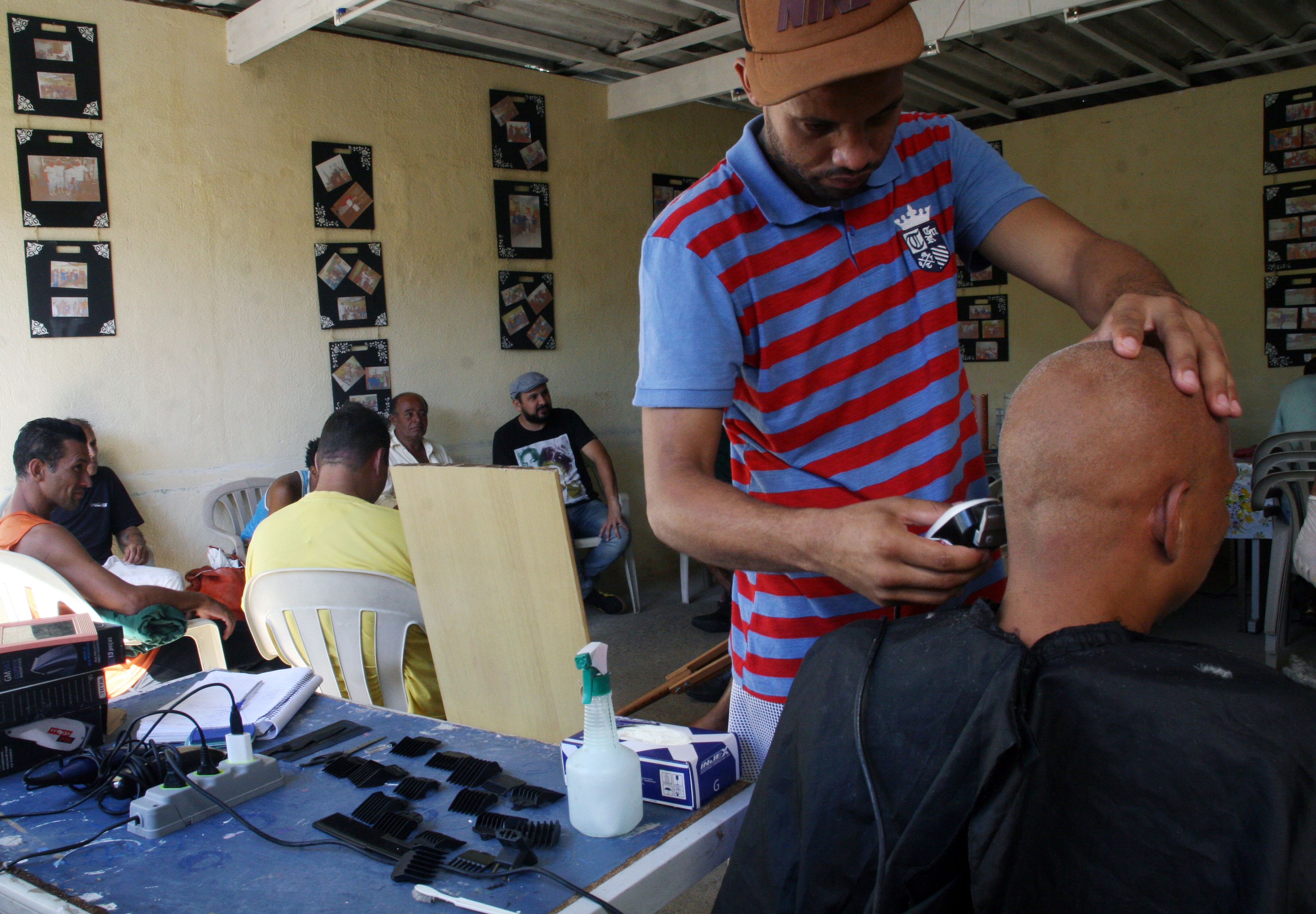 Foto de um convivente cortando o cabelo de outro convivente durante horário de atendimento na Casa Porto Seguro. No fundo há outros conviventes sentados nas cadeiras conversando.