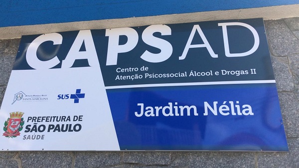 #PraCegoVer: Placa indicativa, azul e branca, da fachada do CAPS Jardim Nélia. 