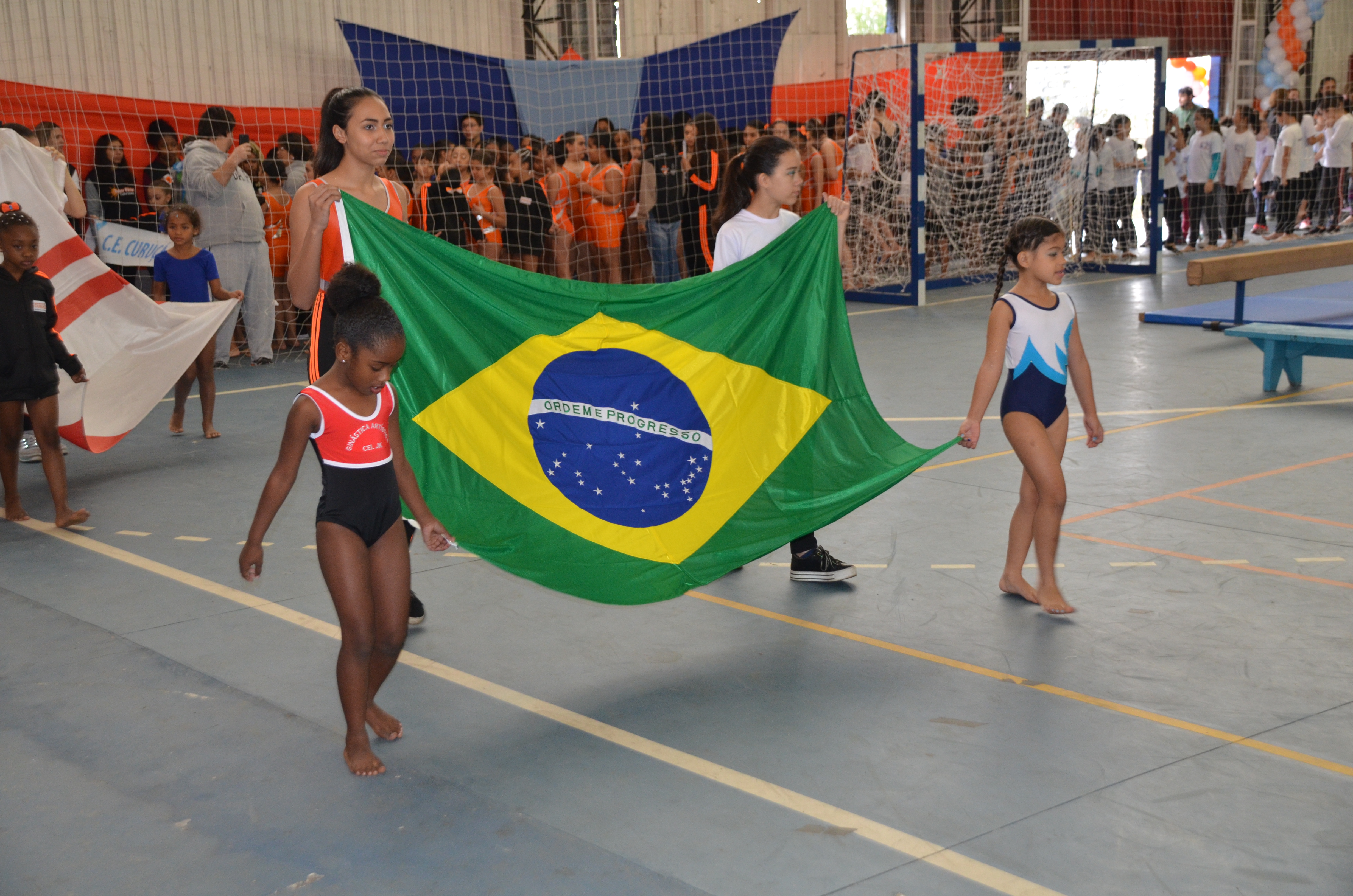 Ginastas do Centro Esportivo JK segurando a bandeira do Brasil dentro da quadra do Ginásio no CERET