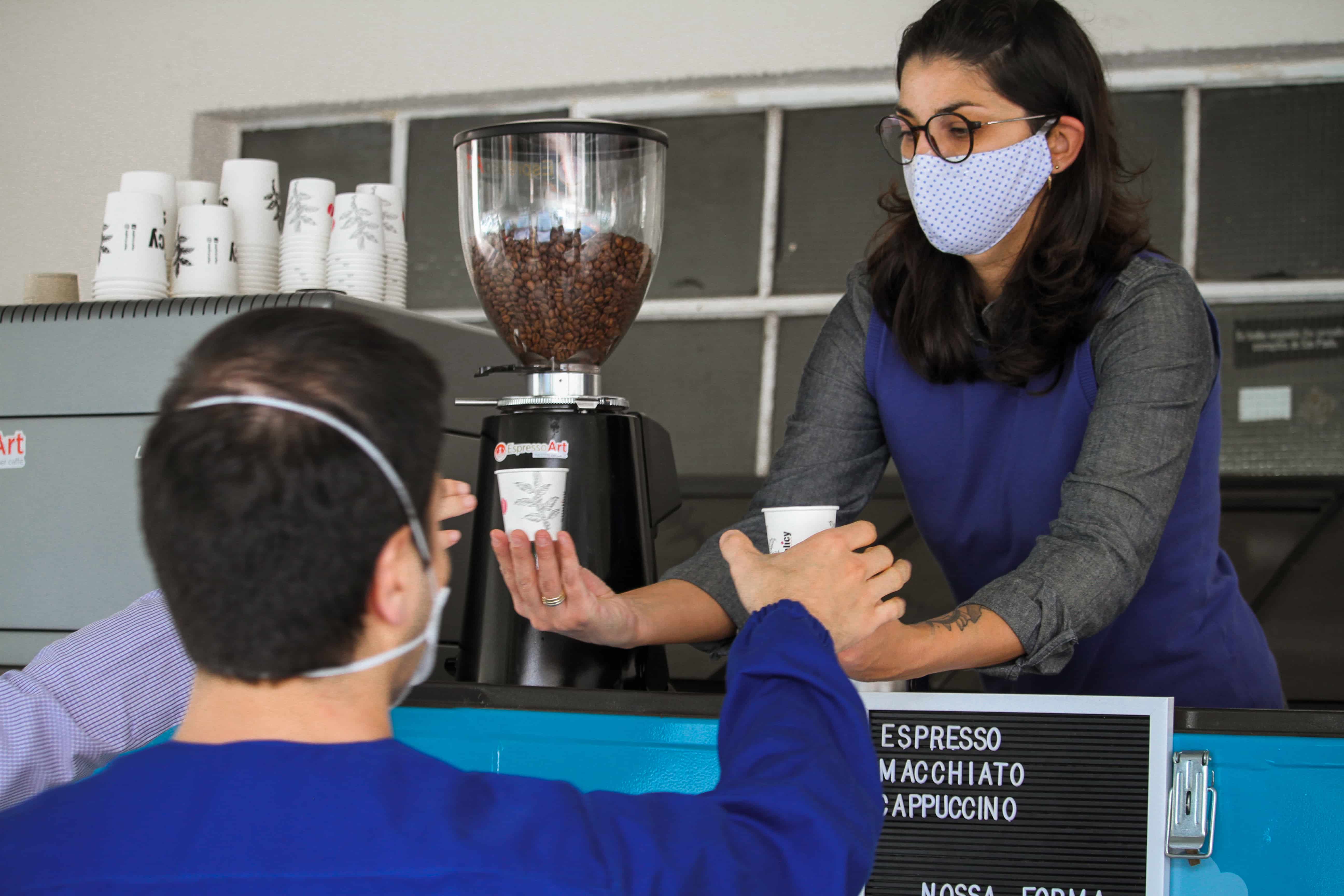 Foto de Viviane Pereira entregando café a duas pessoas. Todos na foto usam máscaras no rosto.