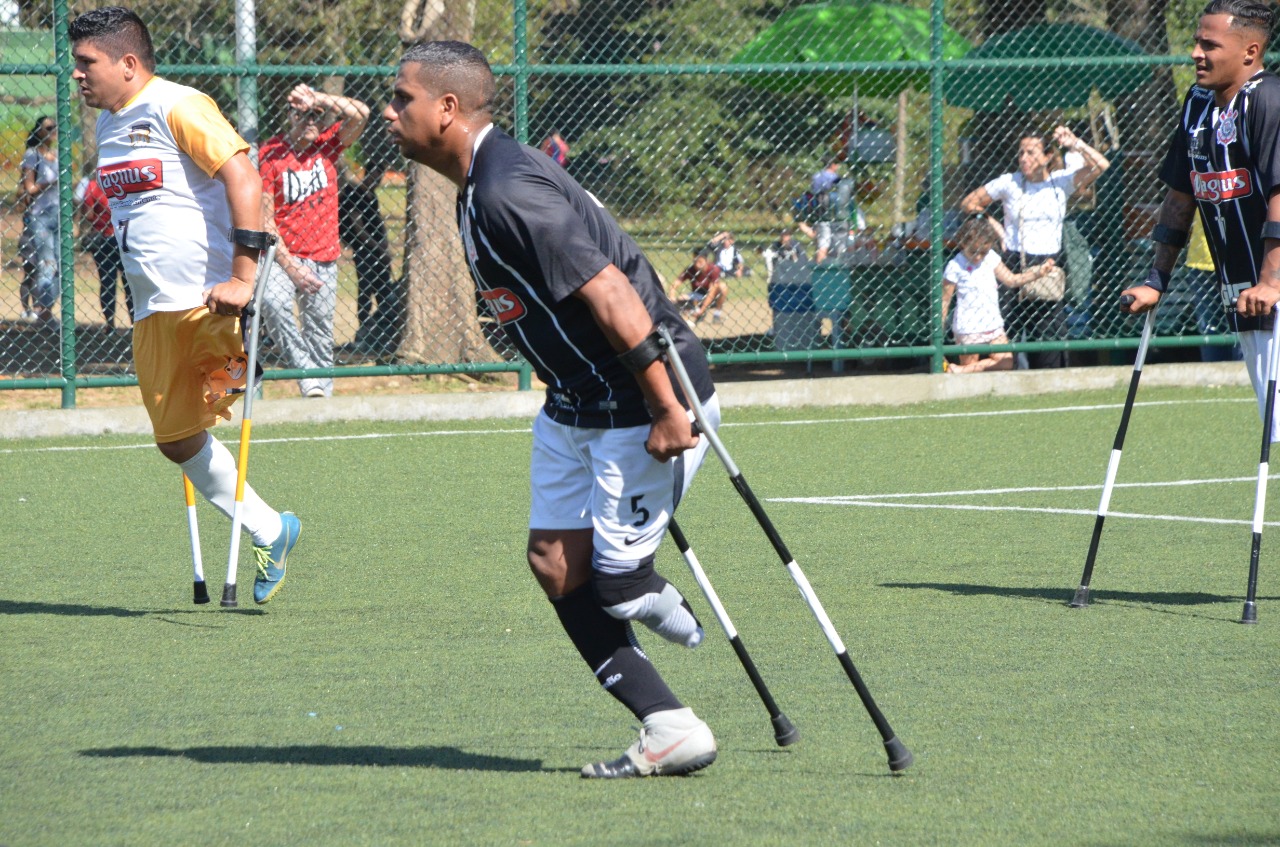 Jogador do Corinthians do Futebol de Amputados movimentando-se com a ajuda de um par de muletas durante partida contra o Magnus. O jogo é em gramado sintético em um dia ensolarado.