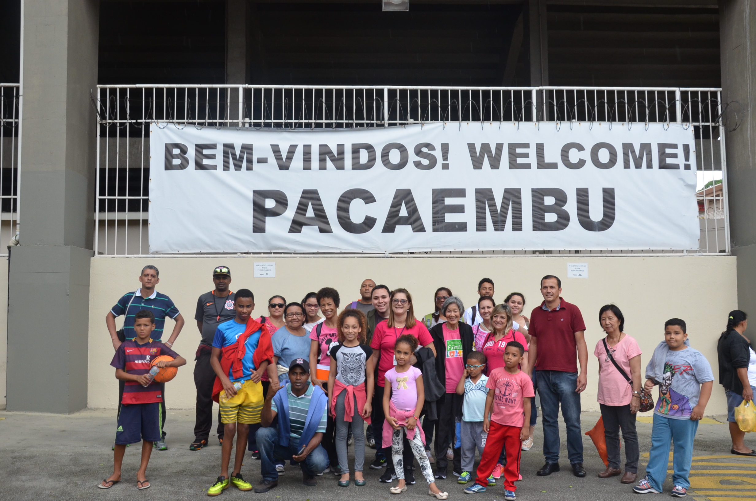 Grupo de pessoas e ao fundo uma placa escrita Bem-vindo! Welcome! Pacaembu