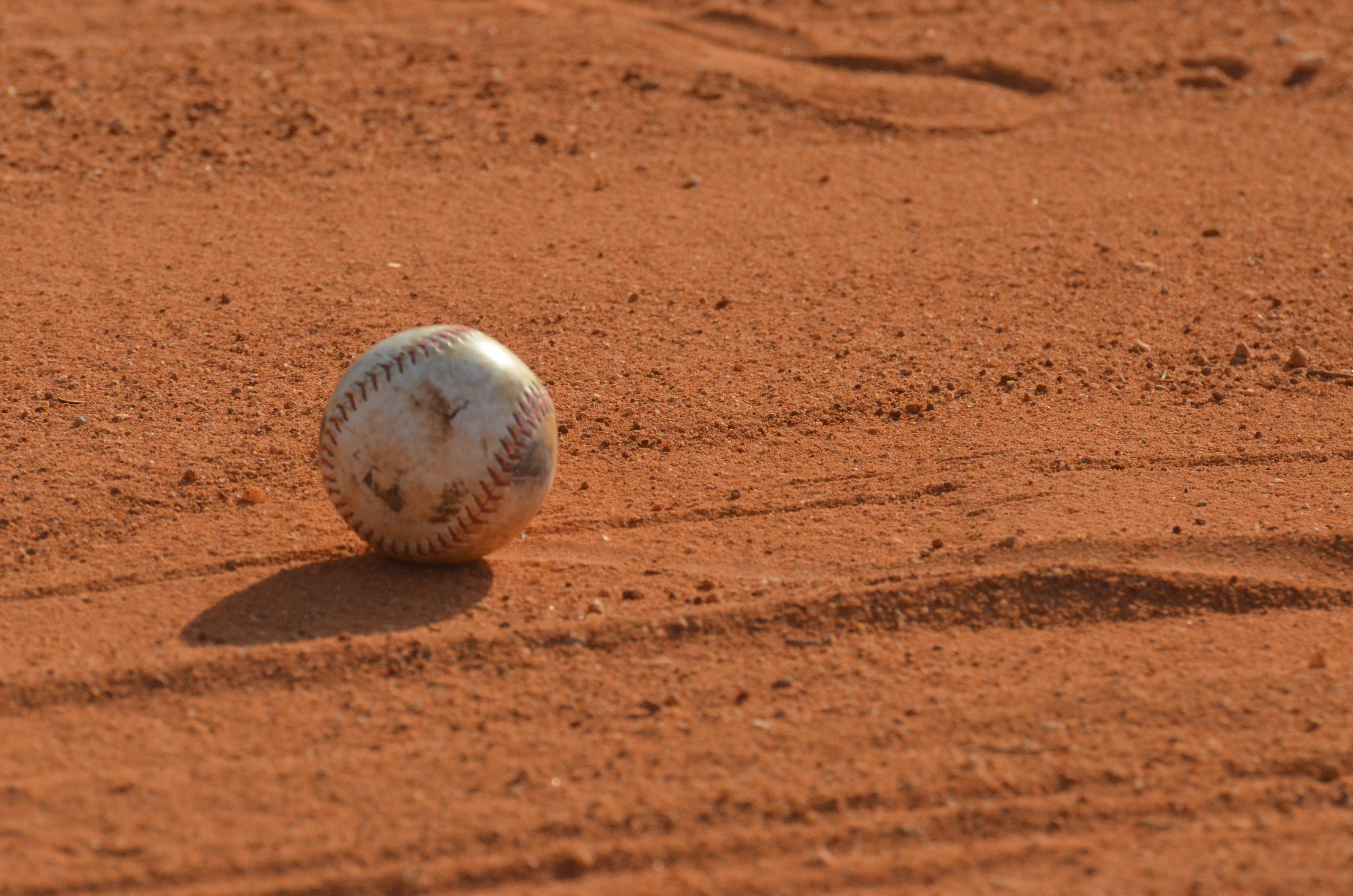 Na imagem, a foto em plano fechado, mostra uma bolinha de beisebol sobre a areia