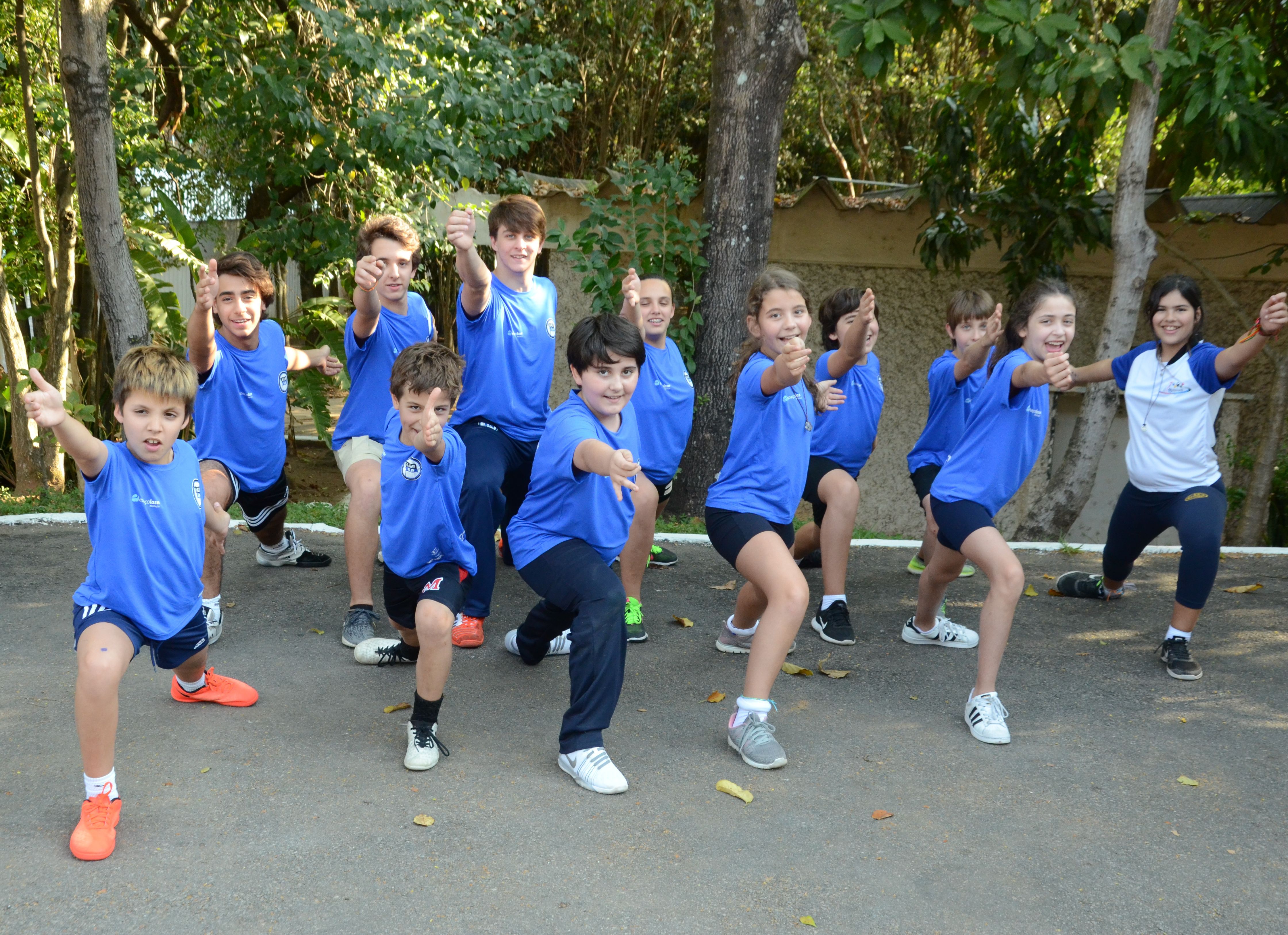 Na imagem, aparecem crianças vestidas com uniforme azul fazendo um movimento com braço, típico da esgrima.
