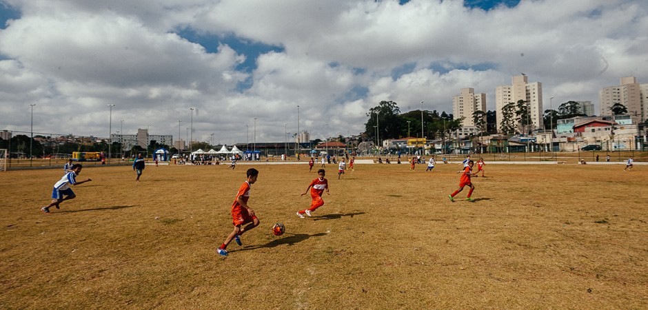 Foto de várias crianças da comunidade jogando bola no campo de terra da área de lazer Água Espraiada