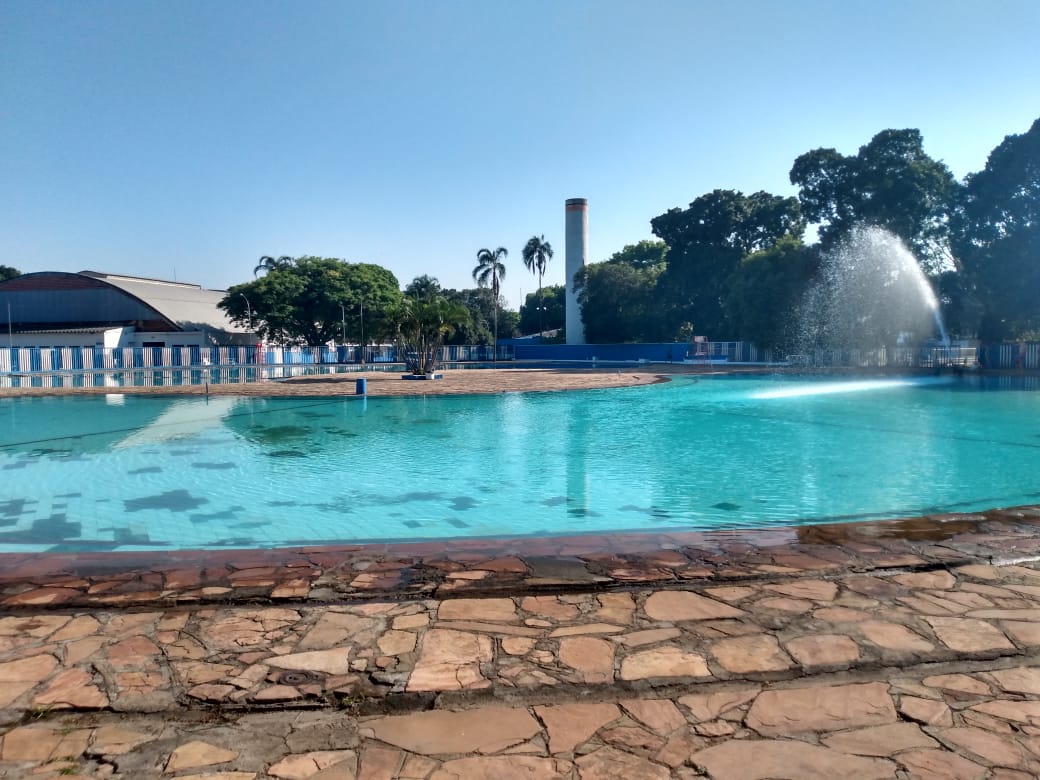 Foto da piscina de um Centro Esportivo municipal vazia em dia ensolarado.