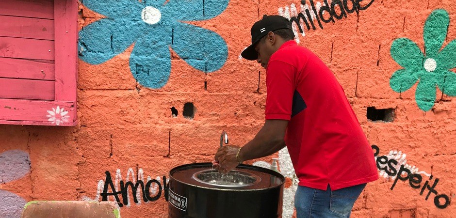 Foto de um morador de uma das comunidades de São Paulo, lavando as mãos em uma das pias instaladas.