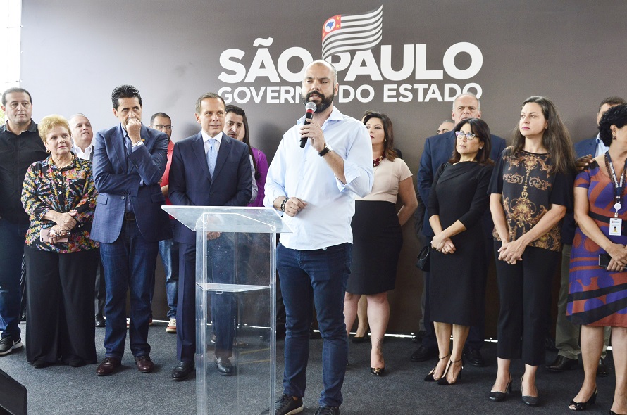 Foto mostra Prefeito Bruno Covas falando ao microfone para outras pessoas em um evento, no mesmo palanque diversas autoridades presenciam a fala do senhor Prefeito.