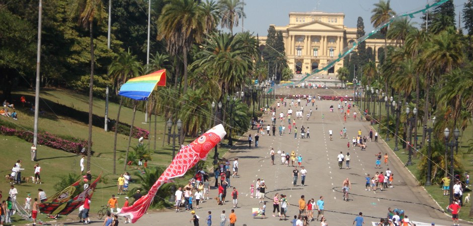 Foto de várias pessoas com pipas coloridas caminhando nos jardins do museu do Ipiranga.