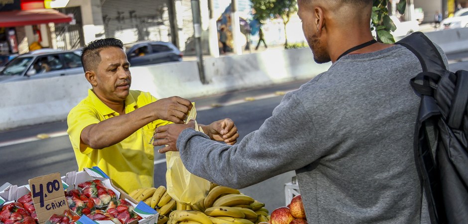 Foto de um feirante e um cliente comprando frutas em uma feira livre.