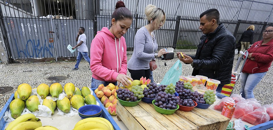 Foto de várias pessoas comprando frutas em uma barraca.