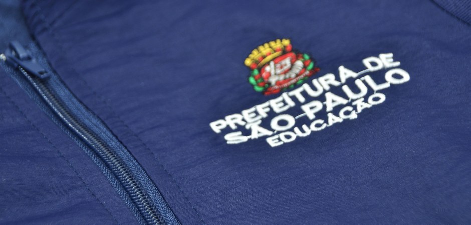 Foto do logo da Cidade de São Paulo em um agasalho de uniforme escolar municipal.