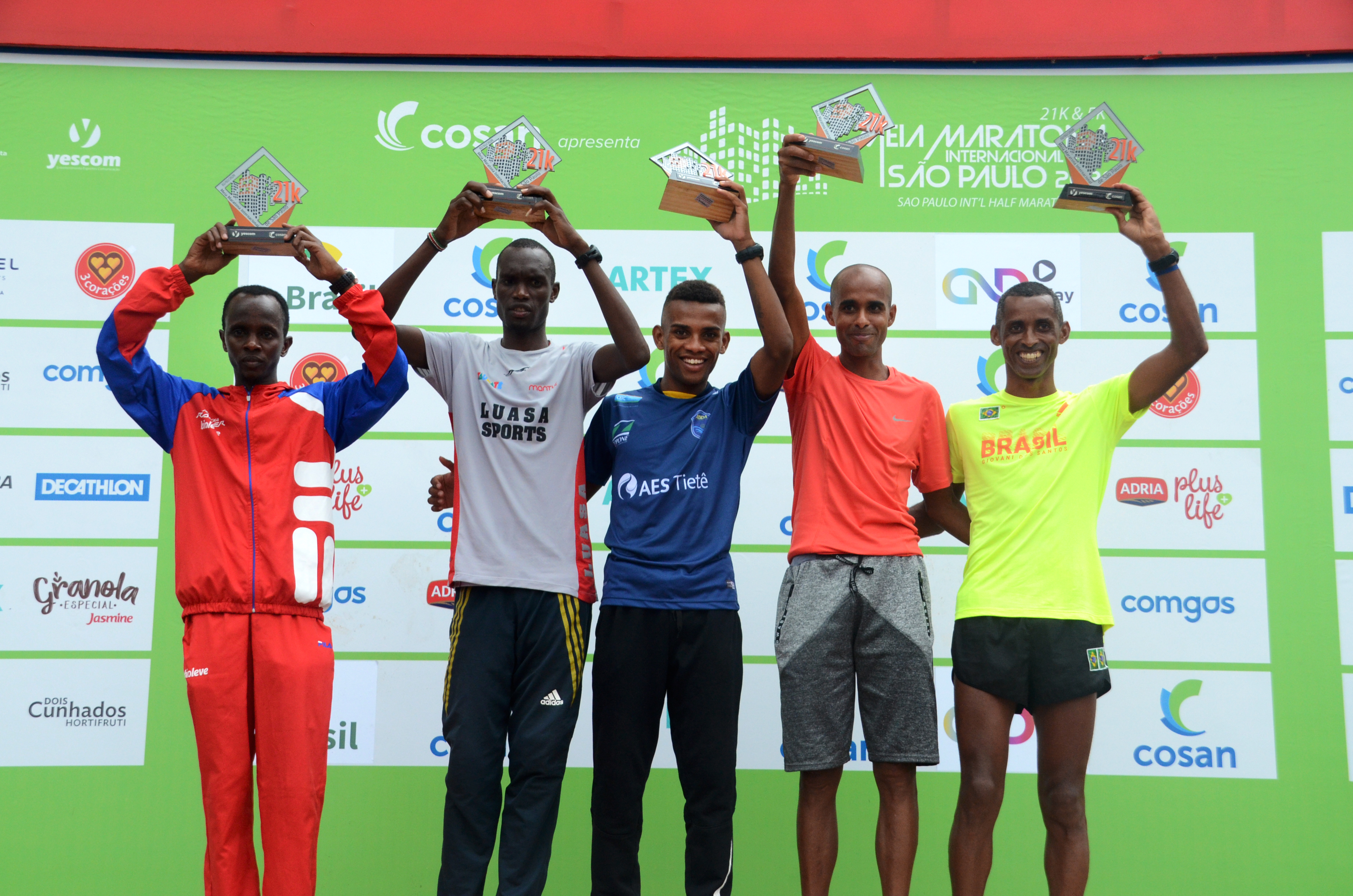 Os cinco melhores colocados da prova masculina de 21 quilômetros fazem pose para foto exibindo seus troféus no pódio.