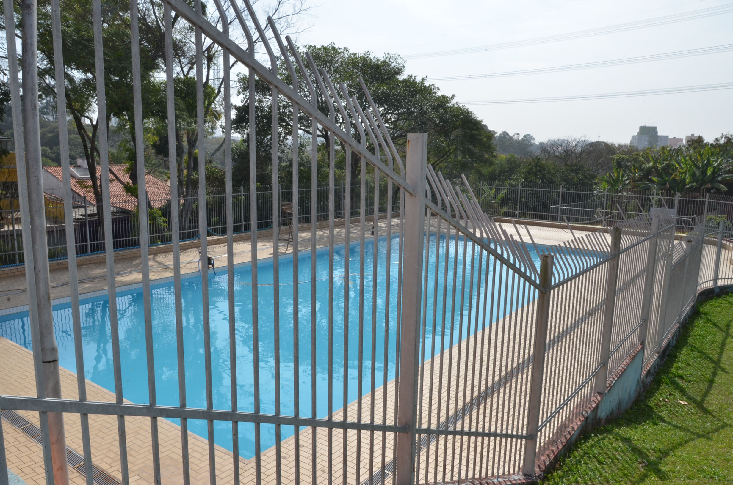 Foto da piscina de um Centro Esportivo municipal vazia em dia ensolarado.
