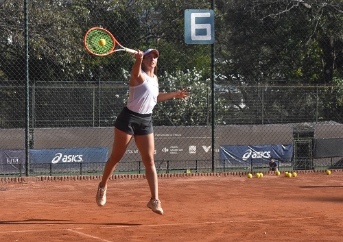 Na imagem, a tenista está saltando e golpeando a bola amarela com a raquete. 
