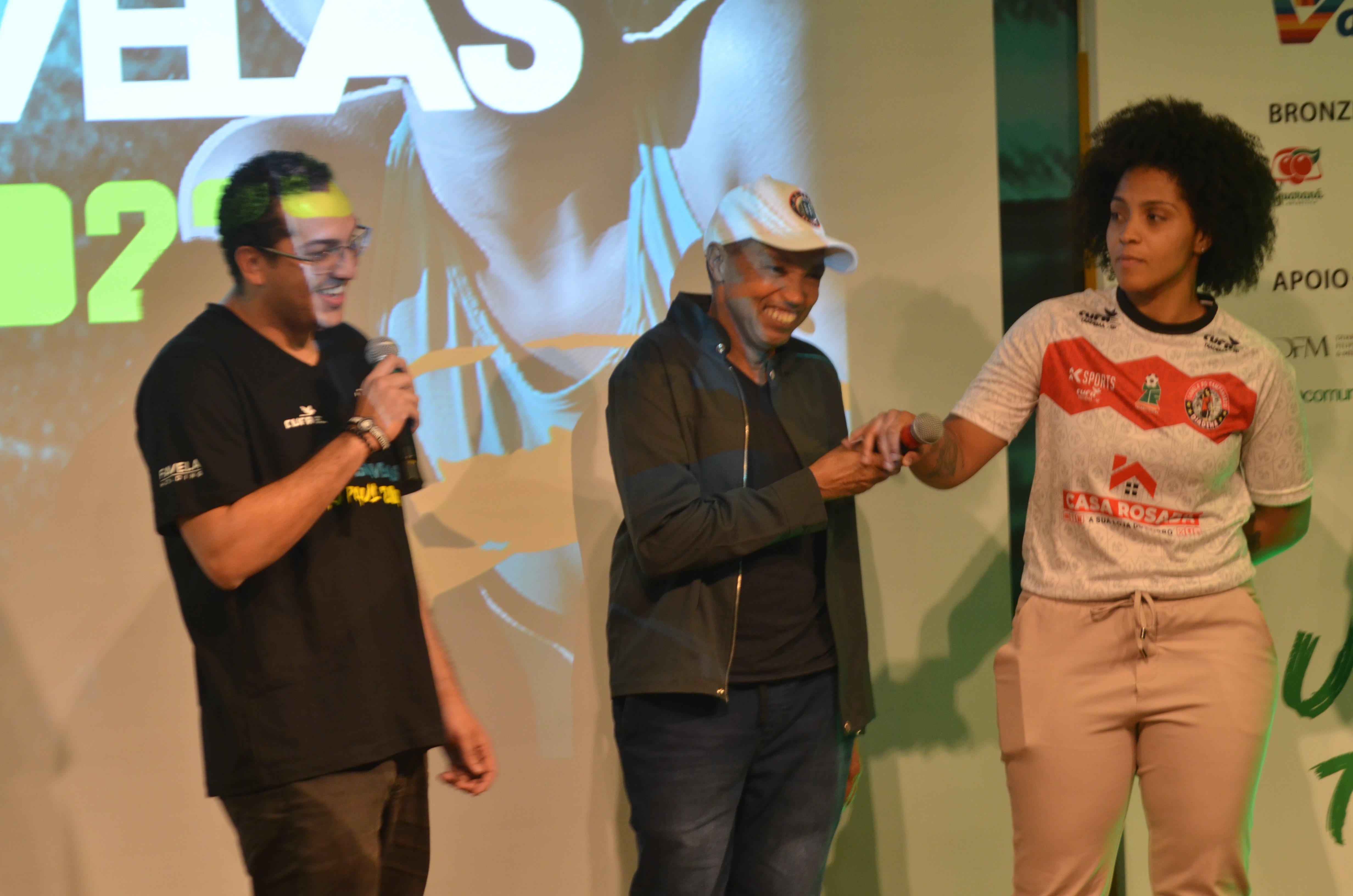Na imagem, apresentador da Taça das Favelas, Pastel treinador campeão da edição 2022, e a jogadora Rayssa.