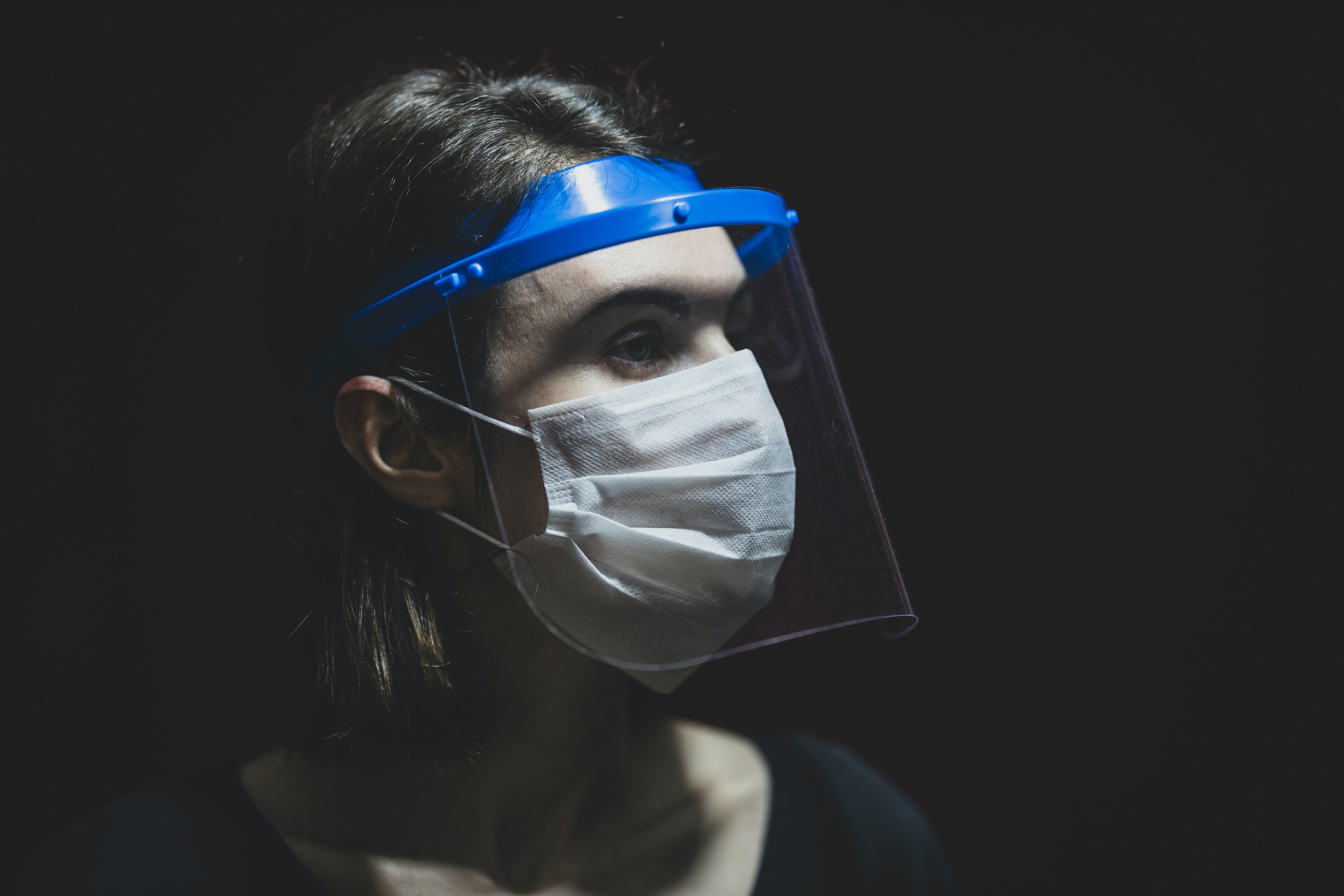 Foto de uma mulher de perfil usando um protetor facial transparente e uma máscara de proteção. 