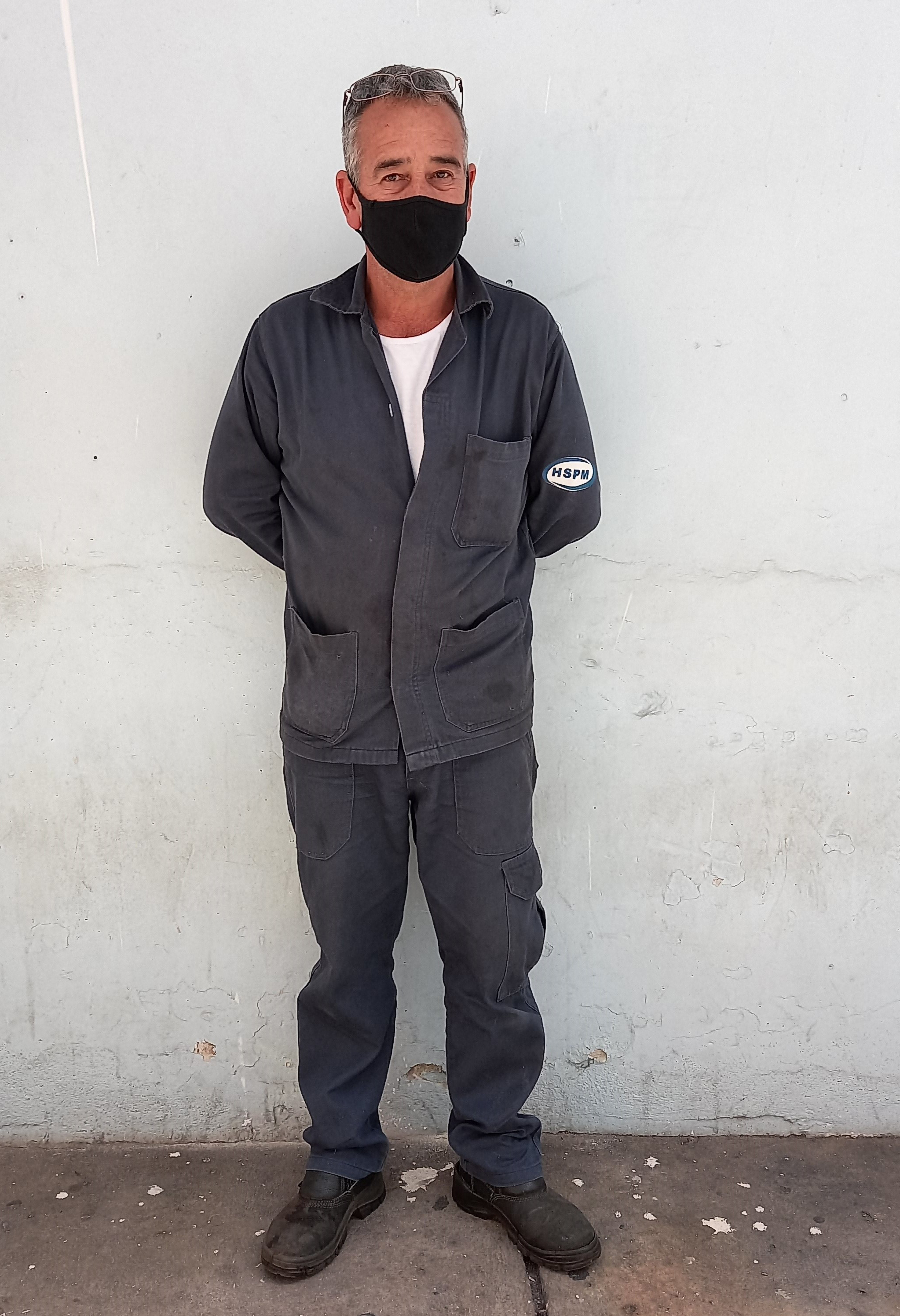 Foto do serralheiro do hospital, de uniforme cinza, em pé em frente a uma parede branca
