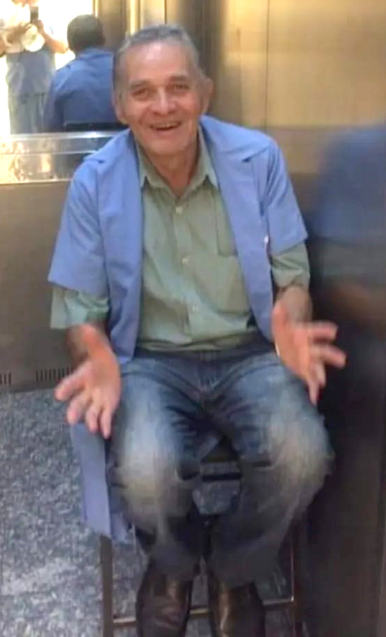 Foto do funcionário sorrindo e sentado em uma banquinho dentro do elevador