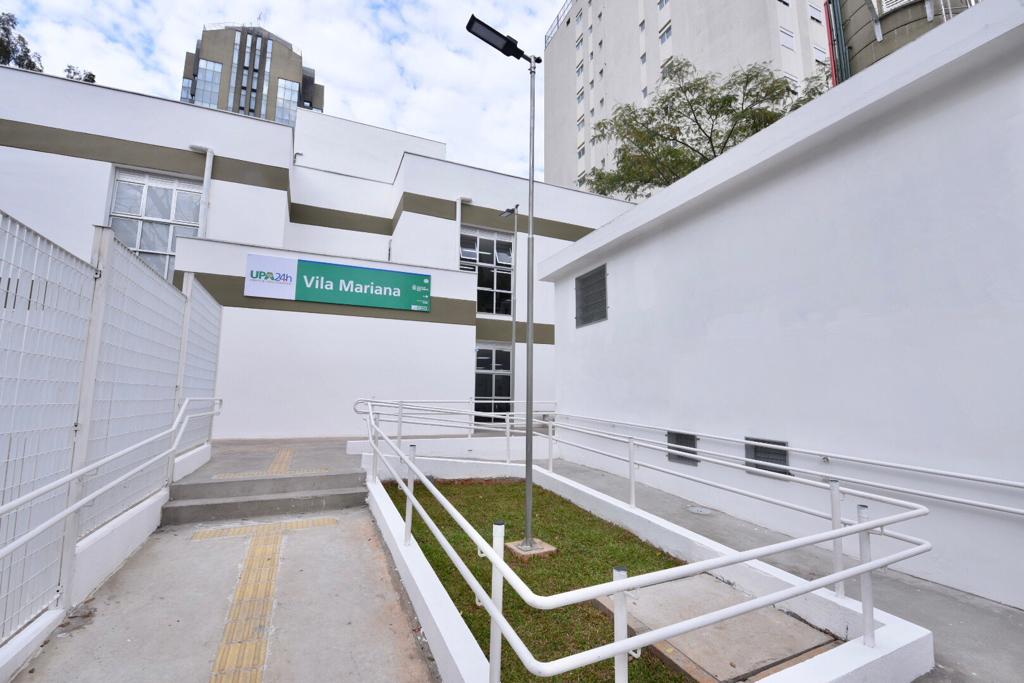 Foto da entrada da UPA Vila Mariana. As paredes são brancas, na fachada há uma placa verde com "UPA 24h Vila Mariana" em letras brancas