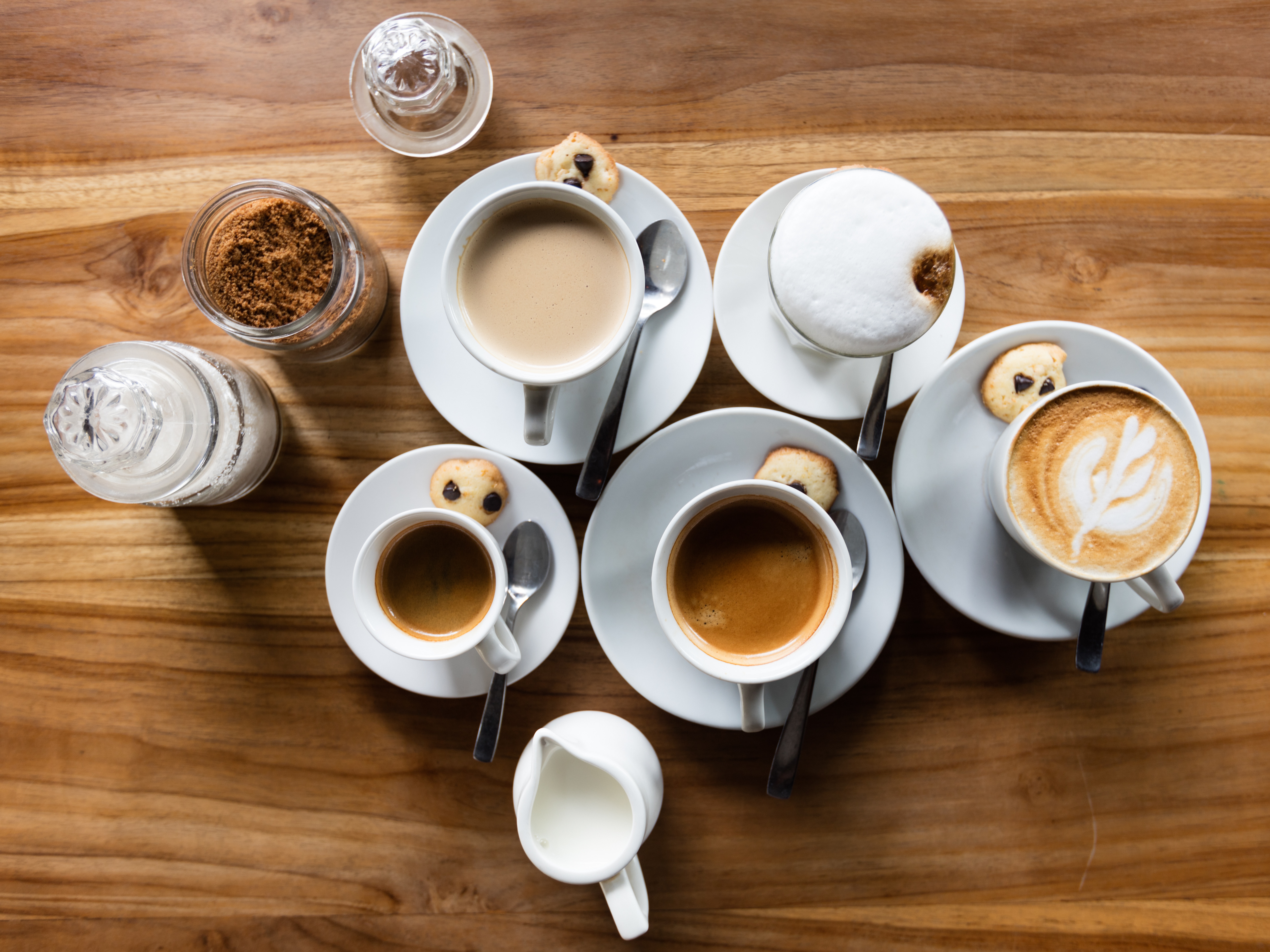 Foto de 5 xícaras de café com o pote de leit, açúcar e canela em volta.