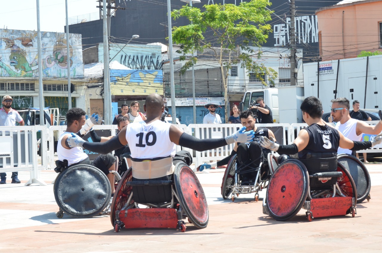Na imagem há seis homens de cadeiras de rodas. Eles estão em um circulo praticando esporte. 