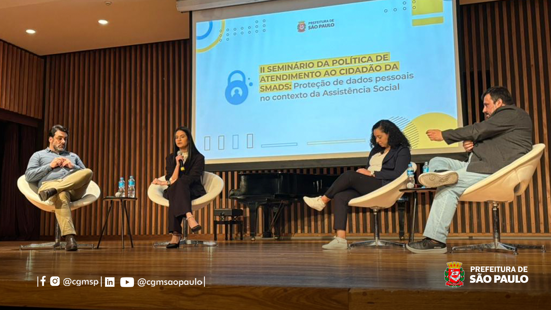 Foto de uma palestra com 4 pessoas no palco