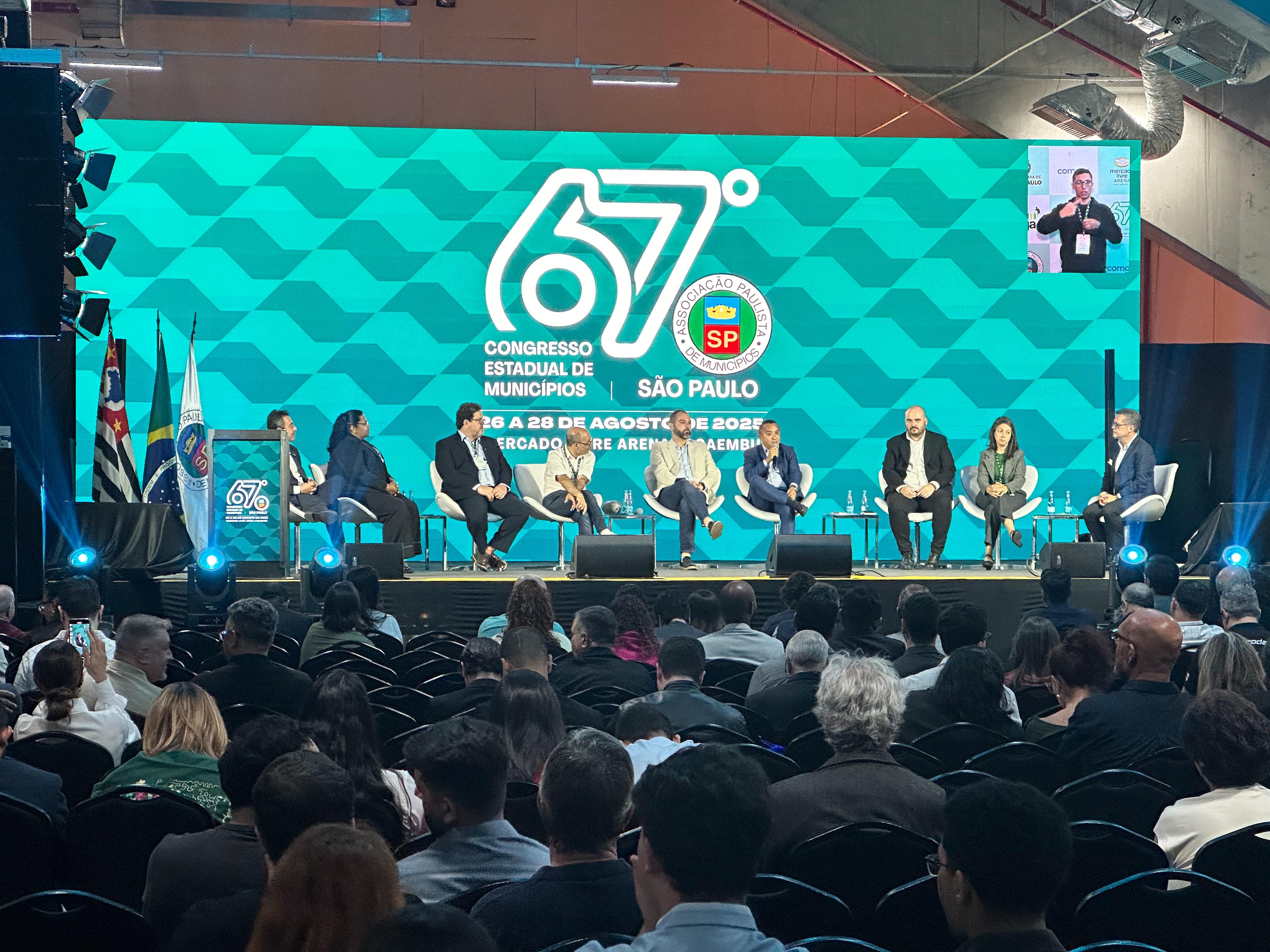 Secretario Sidney Cruz discursando durante o 67º Congresso Estadual de Municípios, ao lado de autoridades convidadas no palco.